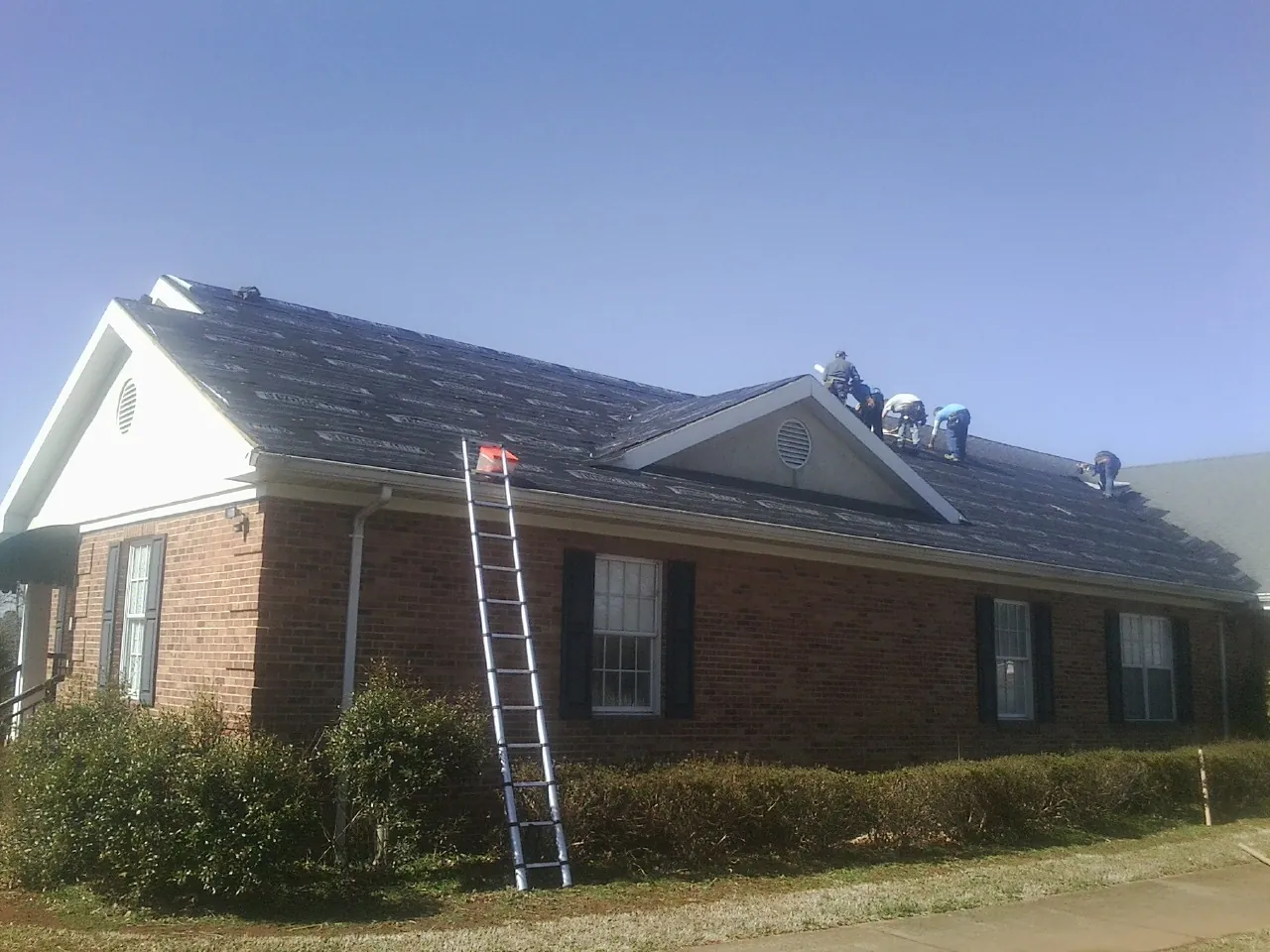 Crew tearing shingles off a brick ranch roof with a ladder set — Emergency Roof Repair work by our crew in Mankato