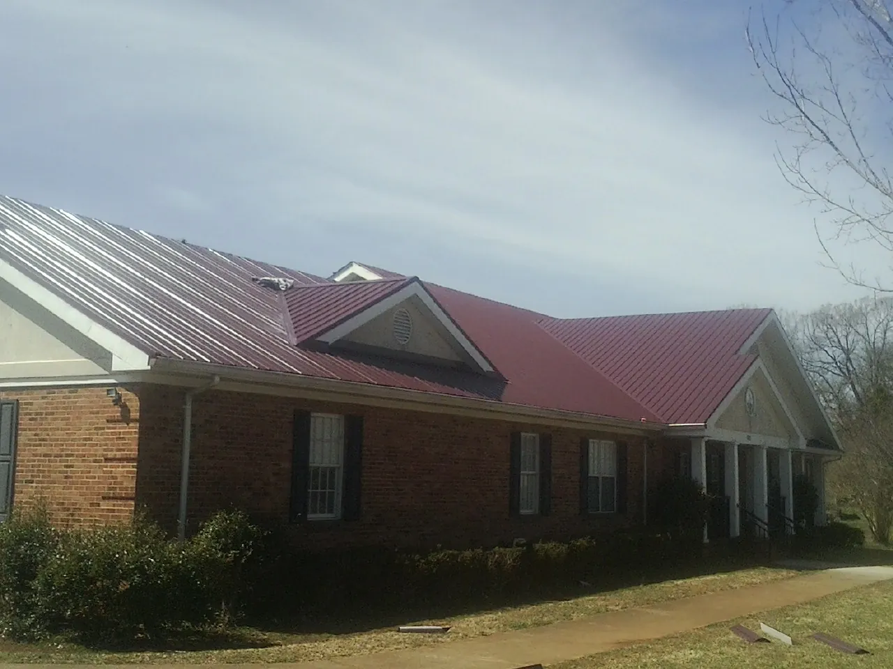 Red metal roof with gabled entries on a long brick building, from a Hail Damage Roof Repair job in Mankato