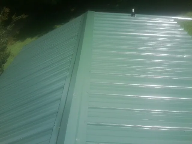 New green metal panels meeting at the ridge of a roof — Flat Roof Repair work by our crew in Mankato
