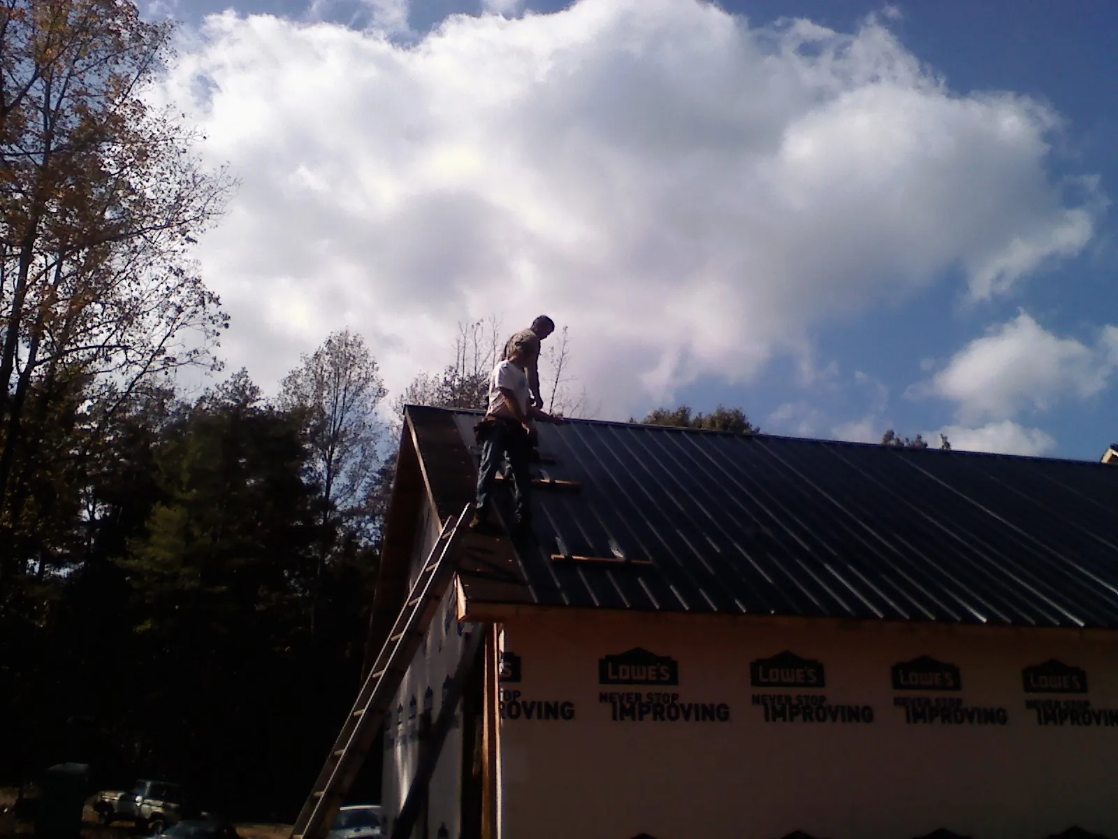 Roofer fastening dark metal panels high against a cloudy sky, from a Roof Inspection job in Mankato